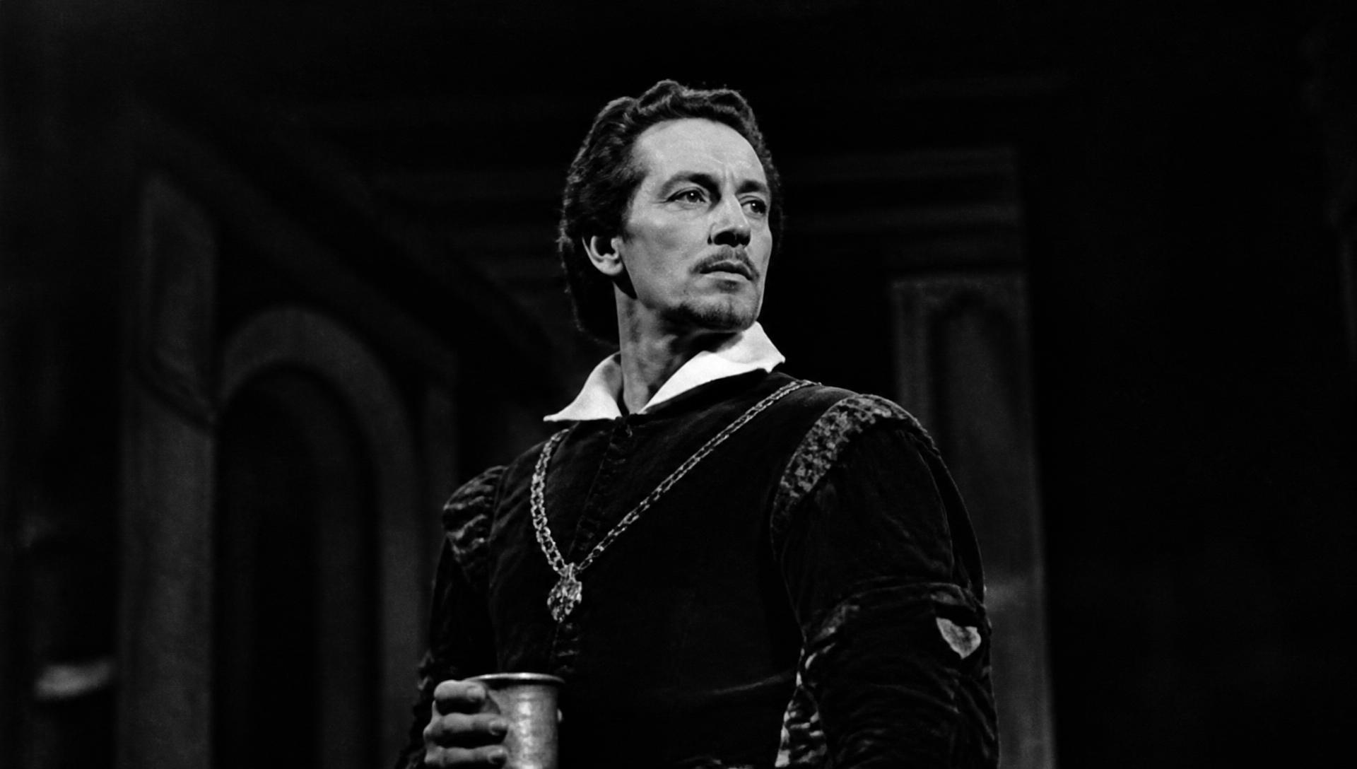 A stage actor in Elizabethan costume lit by a single lamp